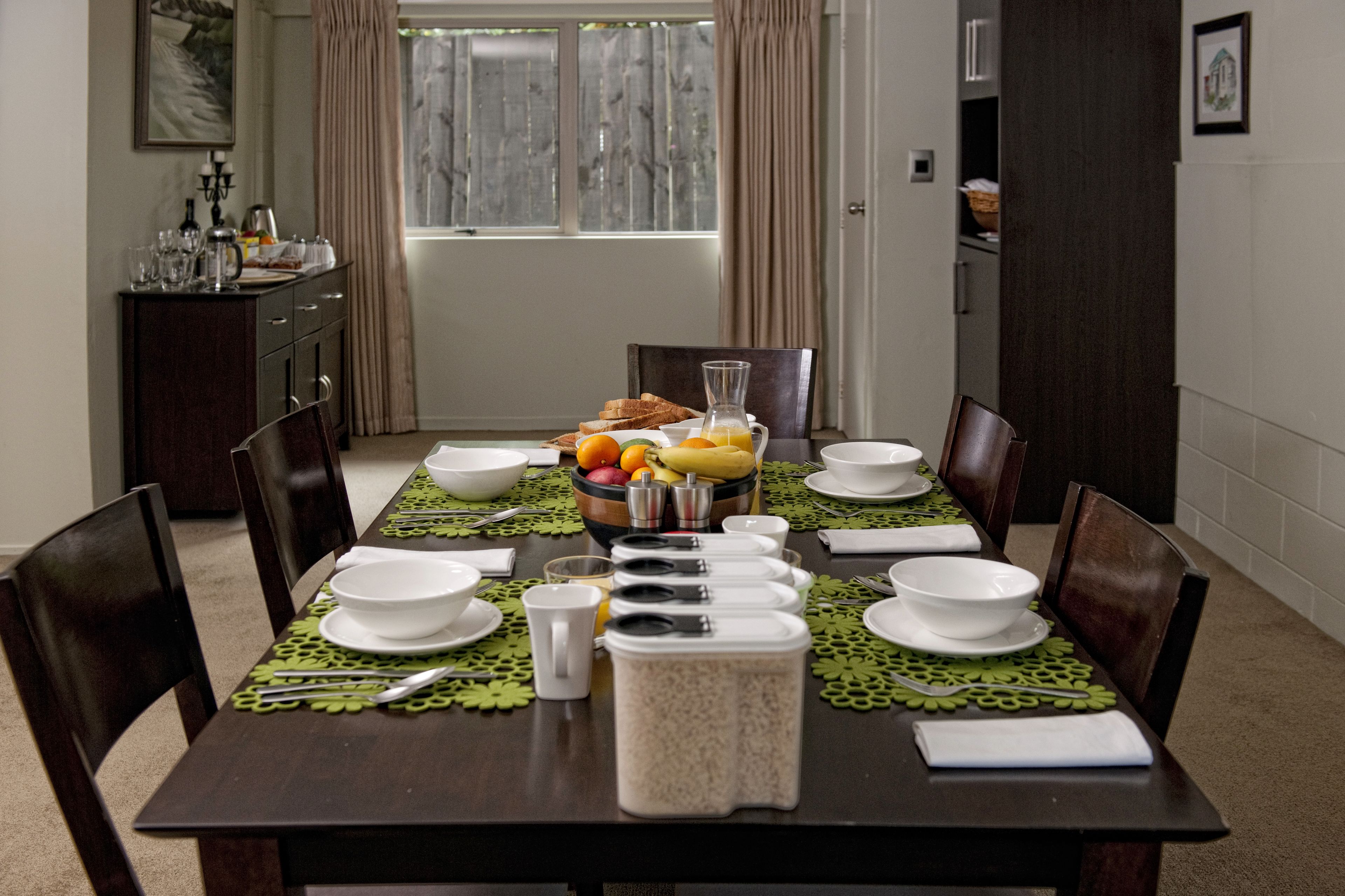 Une table à manger dressée avec de l’assiette blanche, des bols et un pichet de jus d’orange, entourée de chaises.