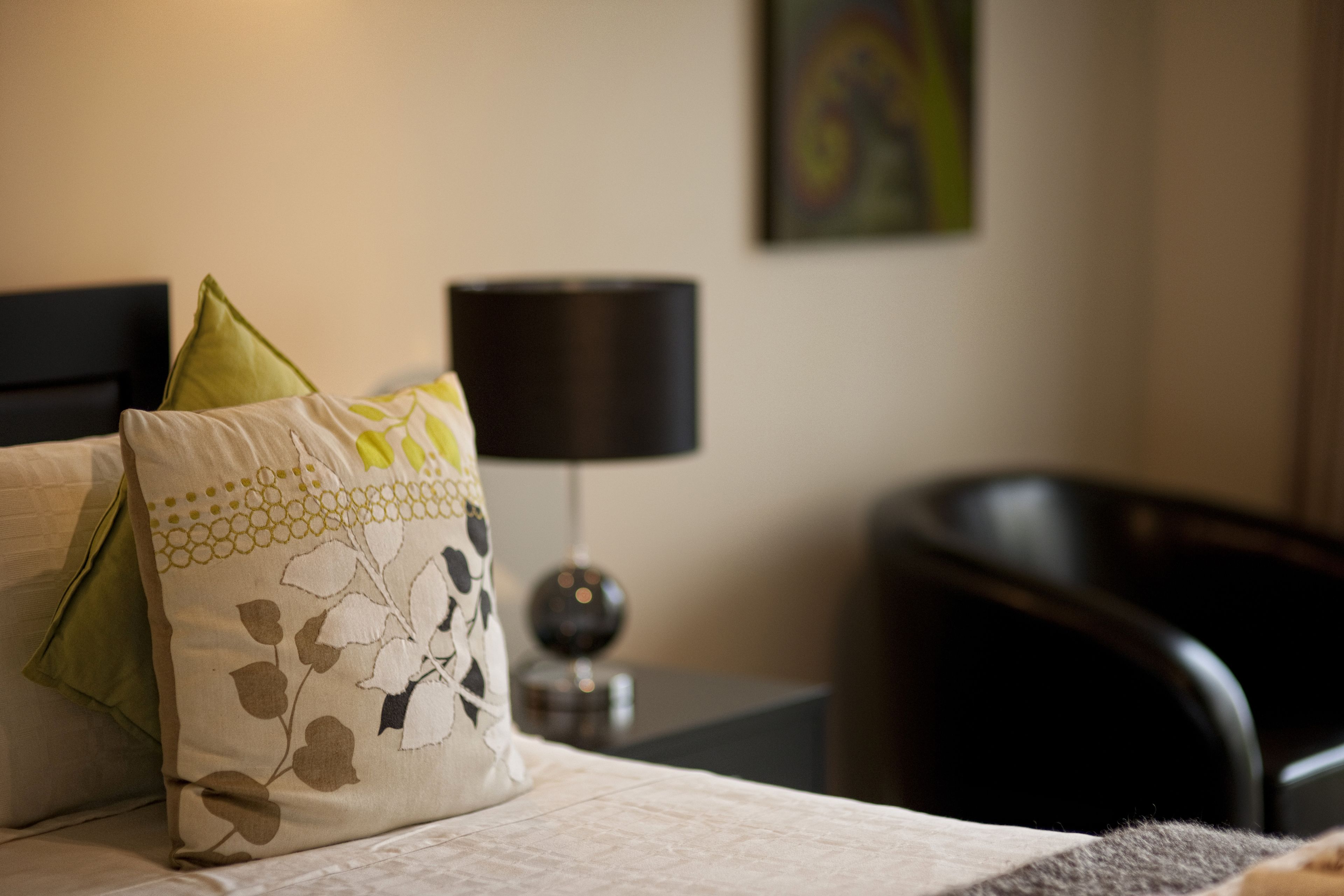 A neatly made bed with decorative pillows, a bedside lamp, and a chair in a hotel room.