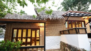 A wooden cabin with a thatched roof, a balcony, and a stone wall.