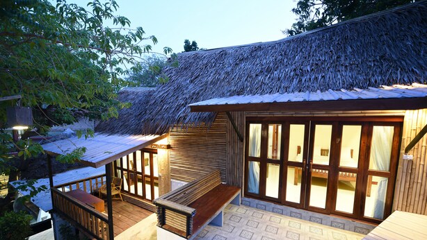 A wooden deck with a bench, a thatched roof, and a large window with curtains.