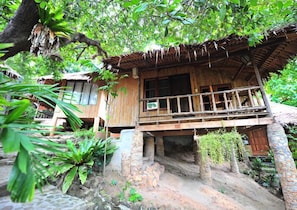 A rustic wooden house with a balcony, surrounded by lush greenery and a stone pathway. - Chunut House Resort (Ko Phi Phi)