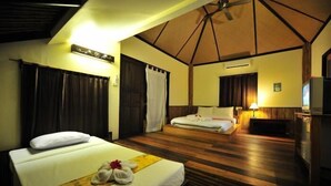 A hotel room with two beds, a wooden floor, a ceiling fan, and a television.