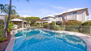 A swimming pool surrounded by a fence, with adjacent buildings and a covered seating area. - Terrapin Apartments (Noosaville)