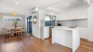 A modern kitchen with white cabinetry, a central island, and a dining area with wooden chairs and a table. - Terrapin Apartments (Noosaville)