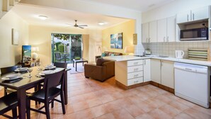 A compact kitchen with a dining area, white cabinets, a microwave, and a dishwasher. - Terrapin Apartments (Noosaville)