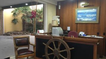 A reception desk with a wooden wheel, a chair, a calendar, and a painting of a sailboat on the wall.