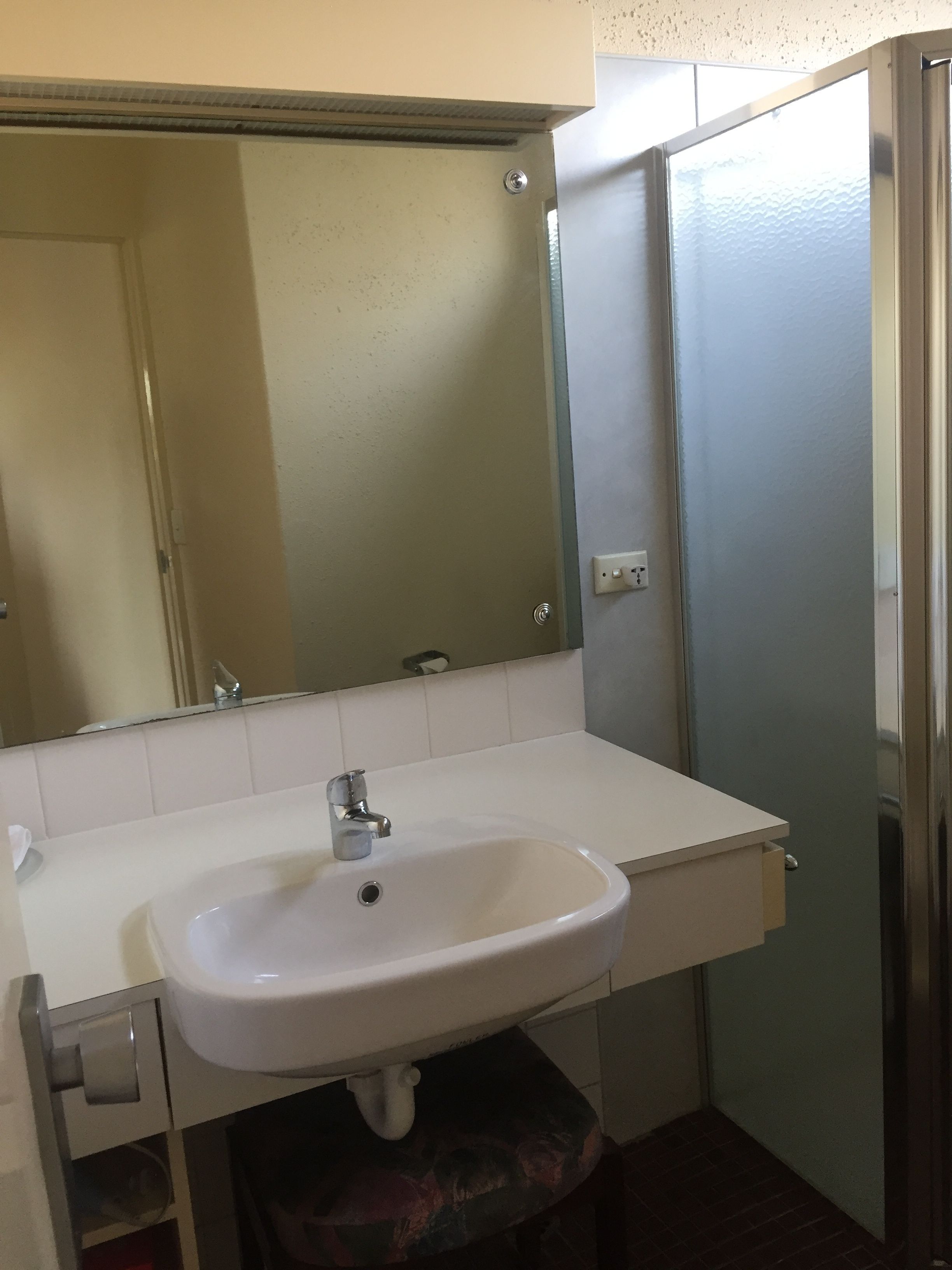 Un baño con un lavamanos blanco, un espejo encima y una puerta a la derecha.