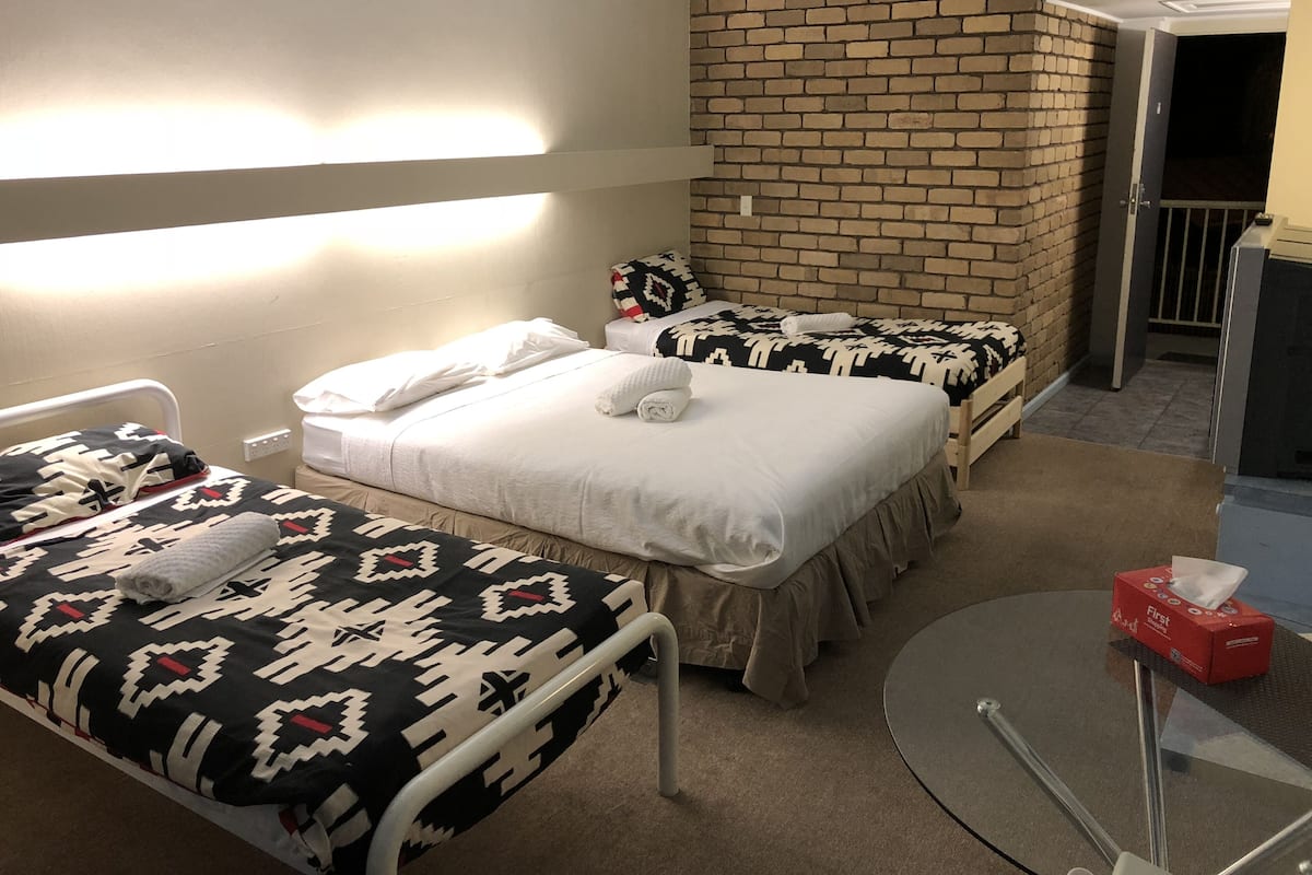 A hotel room with two beds, a brick accent wall, a small table with a tissue box, and a door leading to a balcony.
