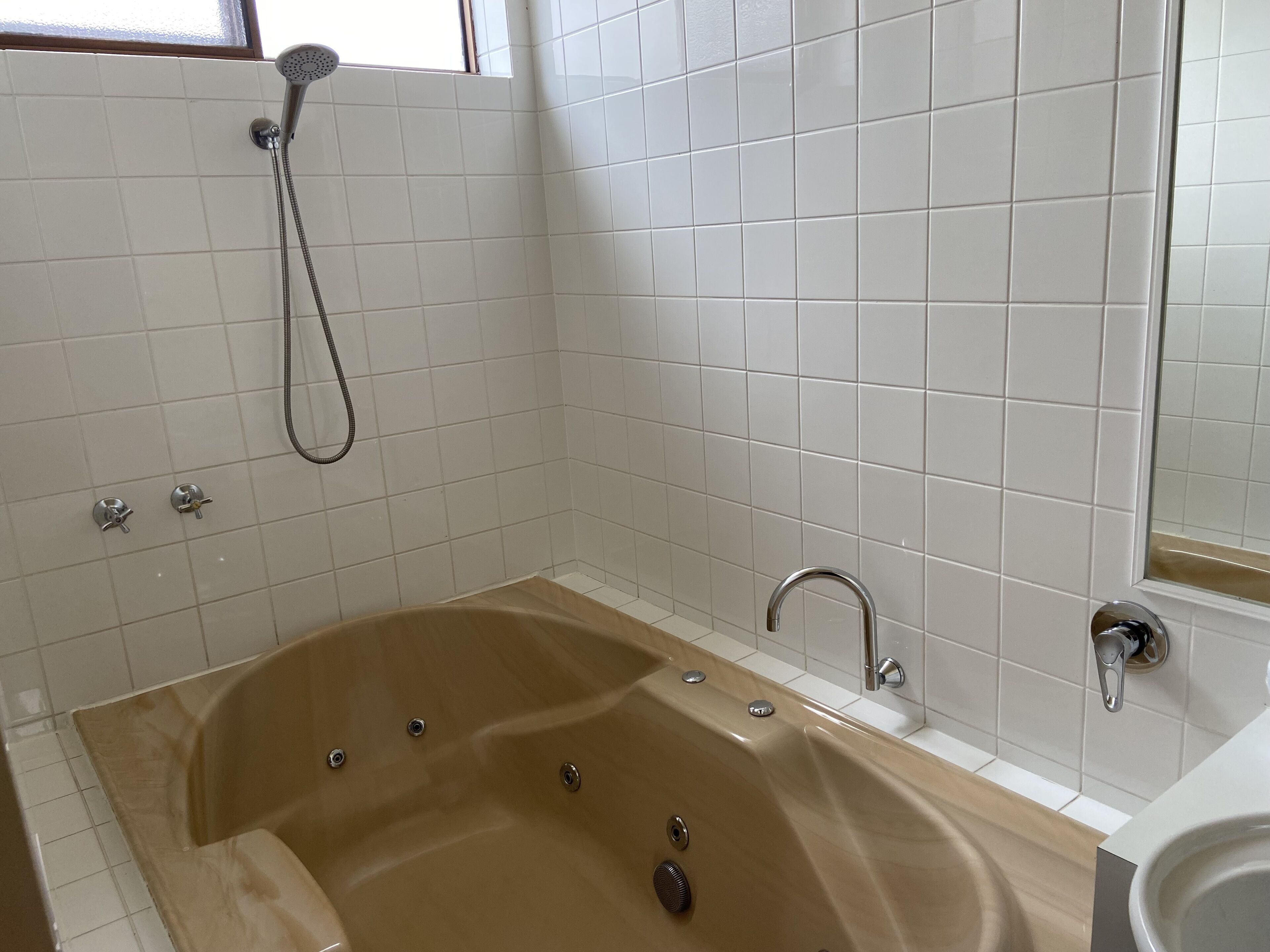 A bathroom with a beige bathtub, a showerhead, and a sink.