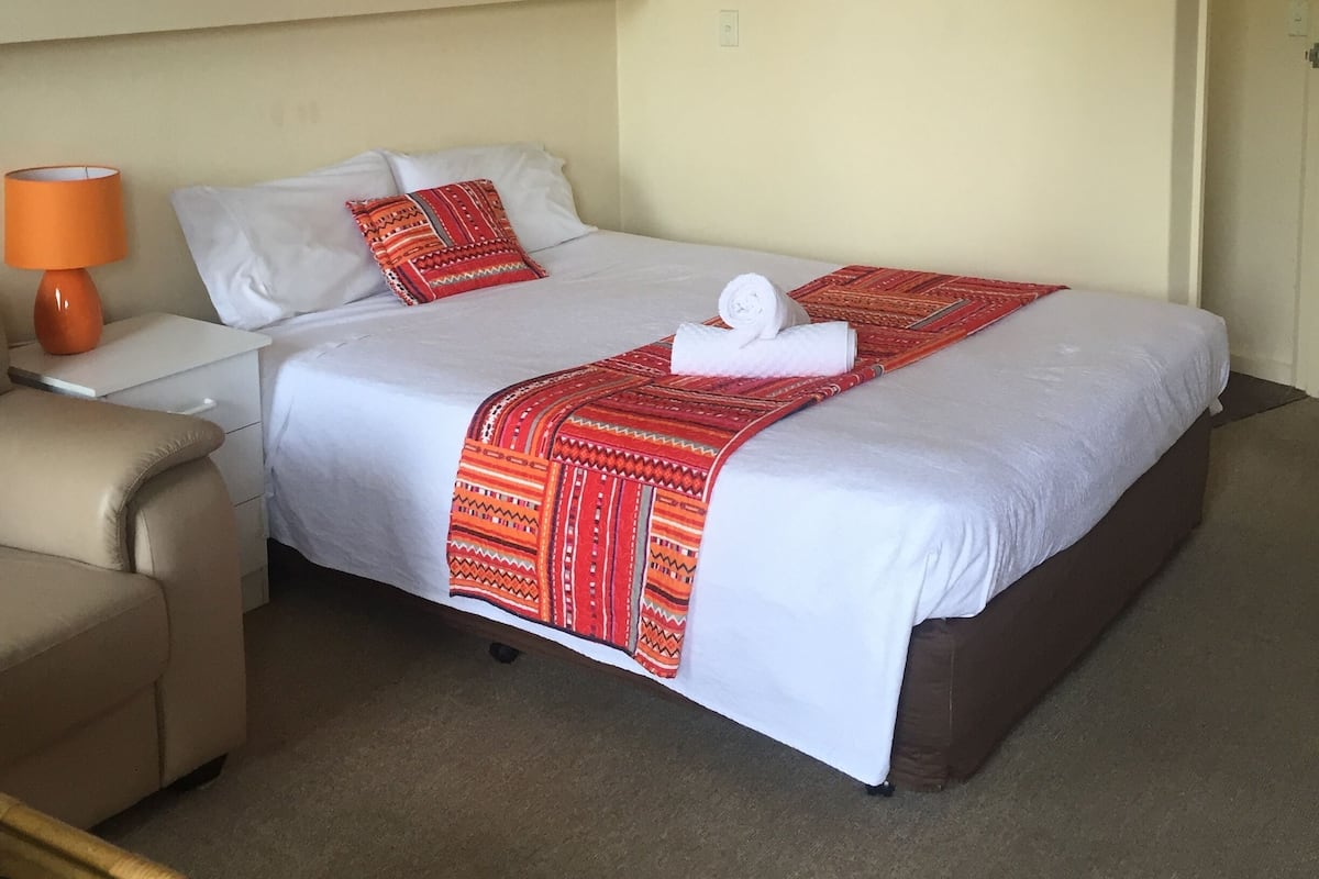 A hotel room with a bed, a chair, a lamp, and a painting on the wall.