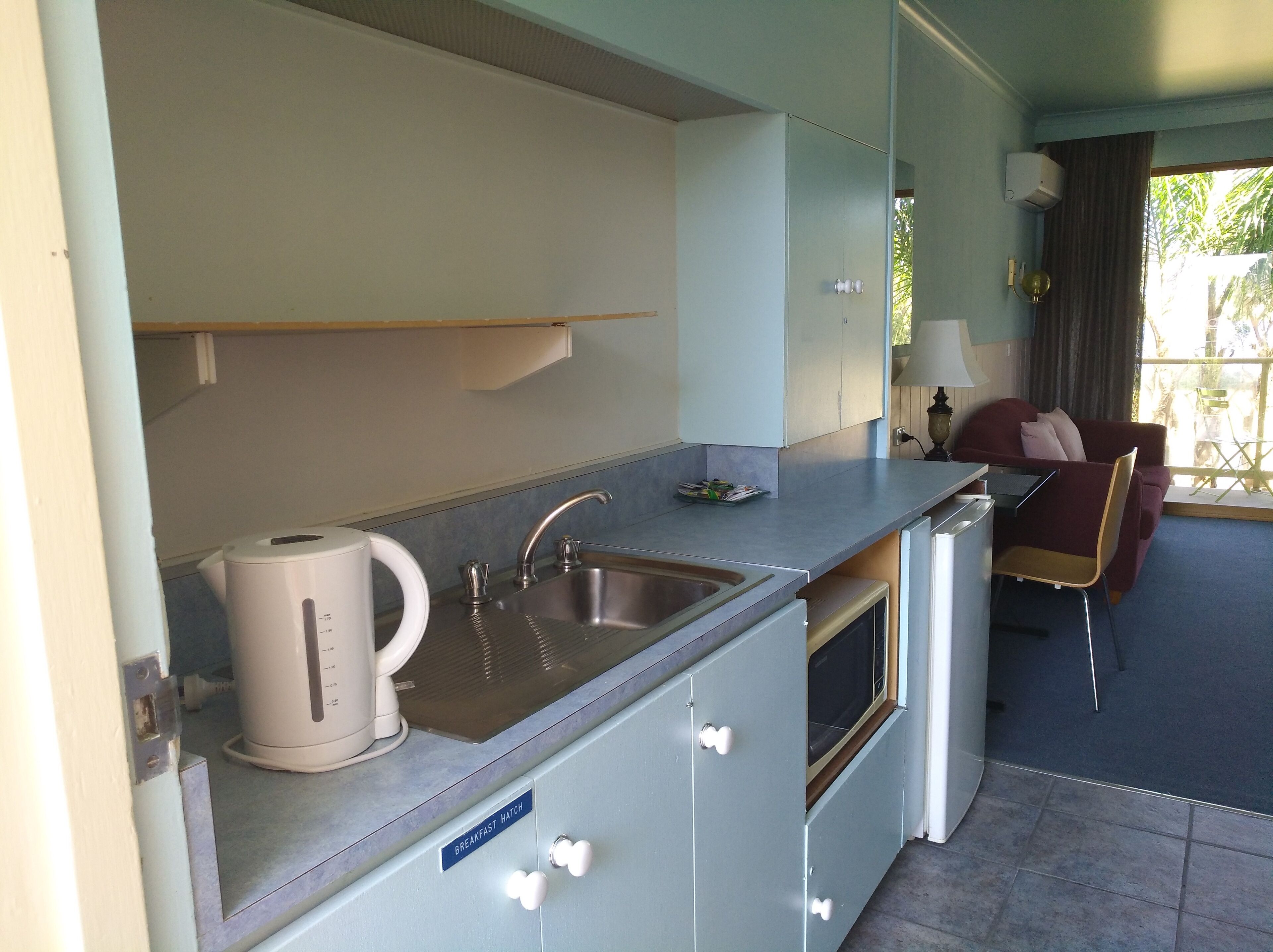 Una kitchenette compacta con cafetera, lavamanos y microondas. Cuenta con una zona de comedor con mesa y sillas, y un sofá.