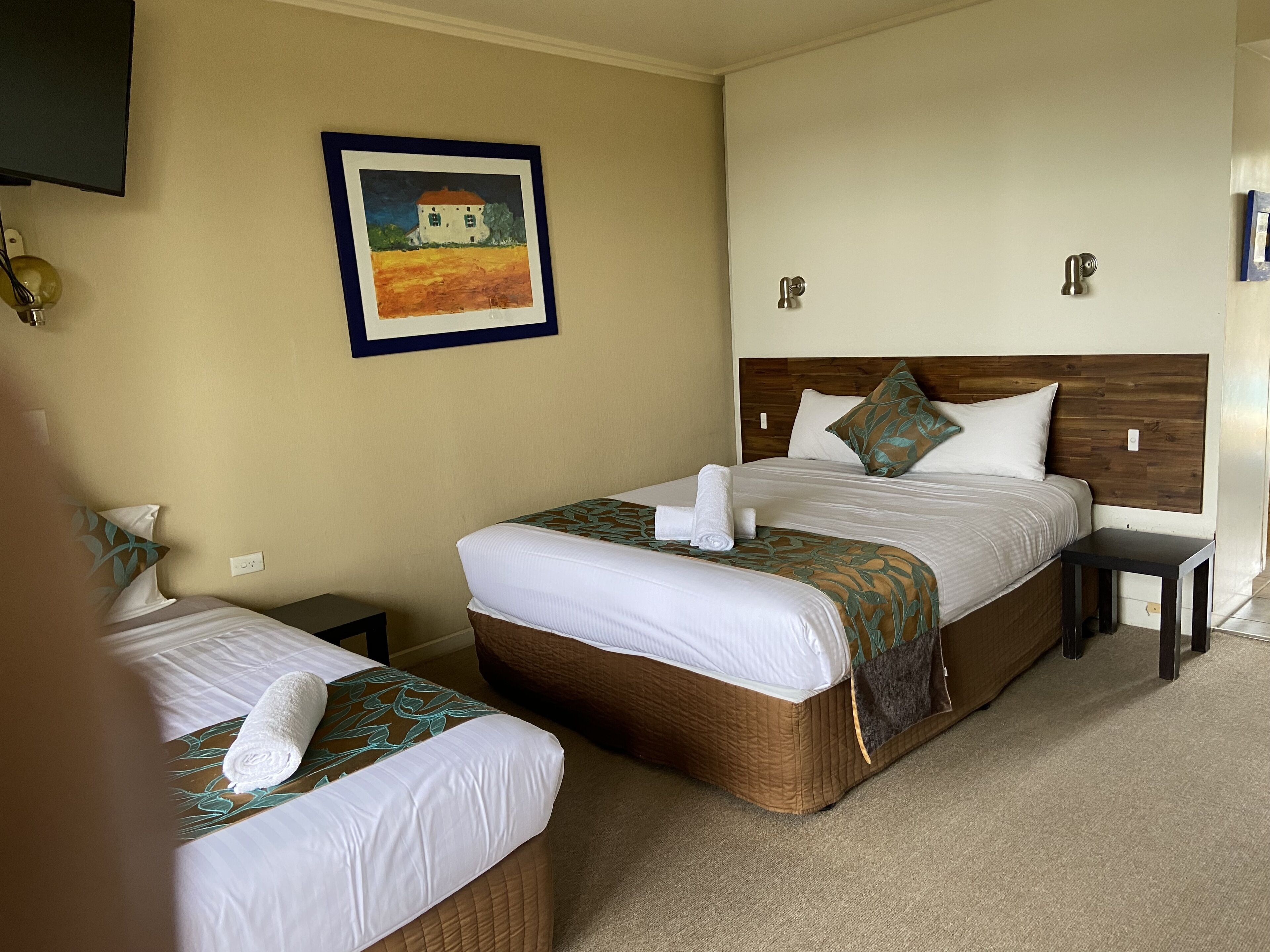 A hotel room with two beds, a painting on the wall, and a small table.