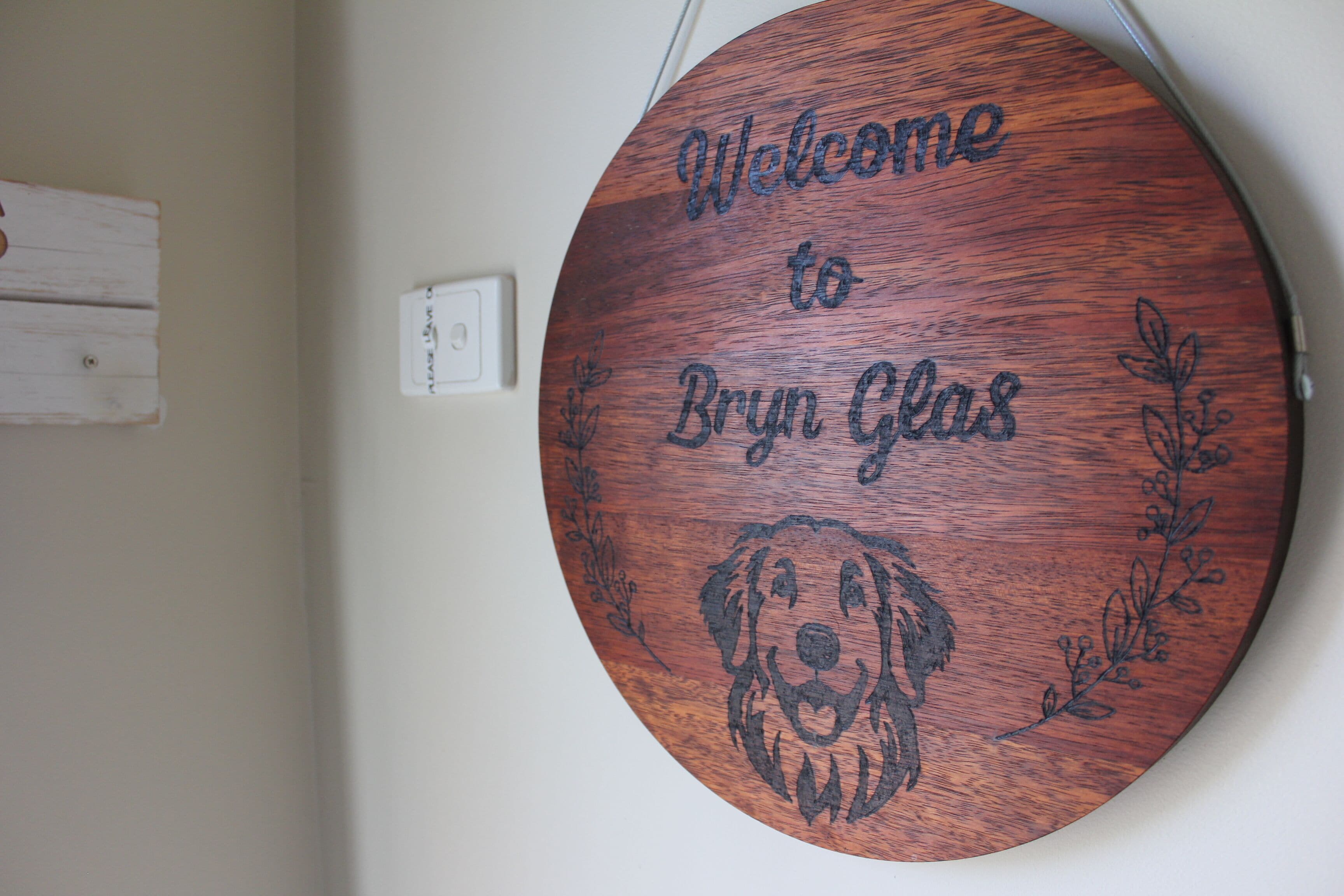 A round wooden sign with a dog engraving and the text "Welcome to Bryn Glas."