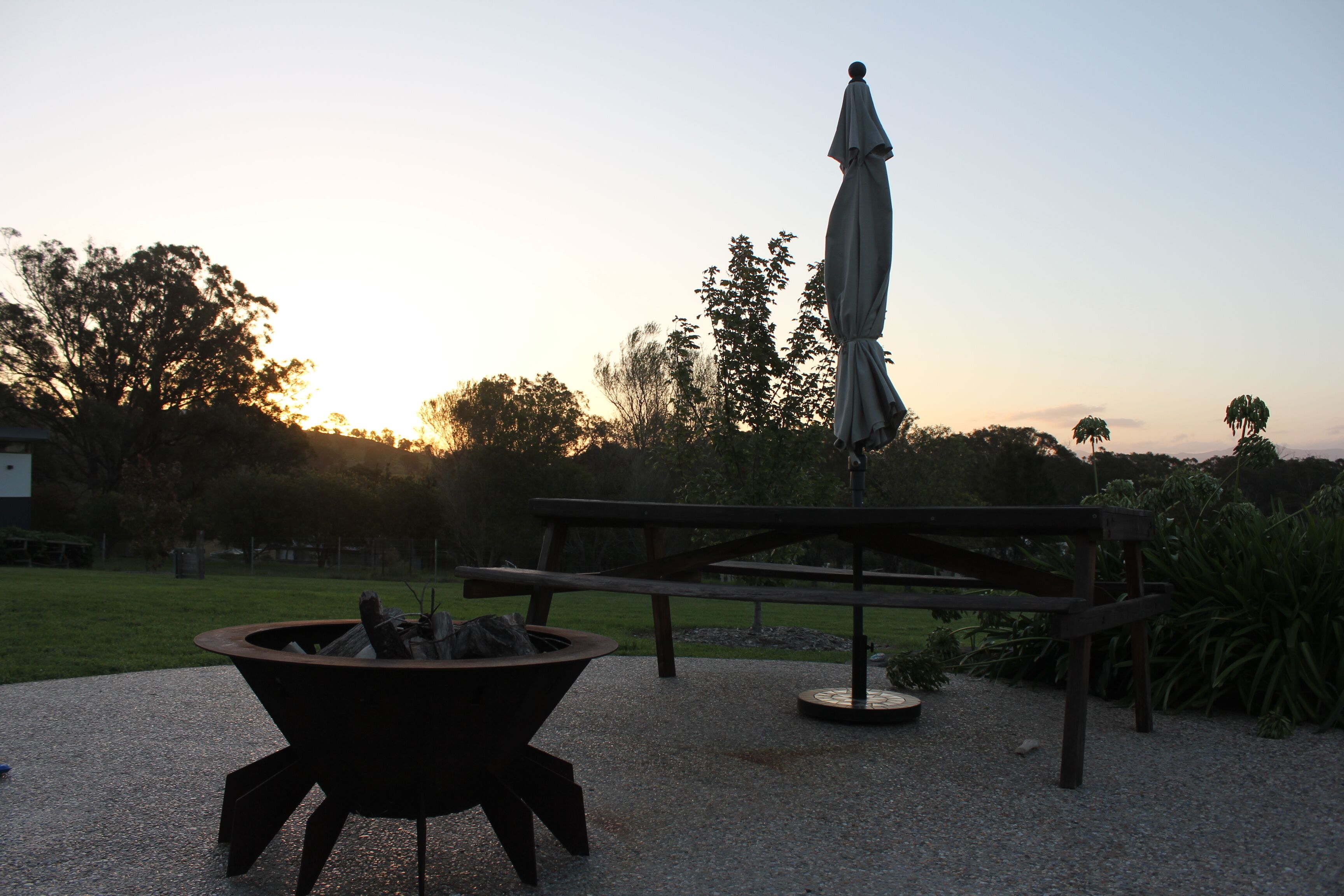 A picnic area with a fire pit, a bench, and an umbrella.