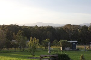 A picnic area with a bench and umbrella, surrounded by a grassy field and trees, with a small building in the background.