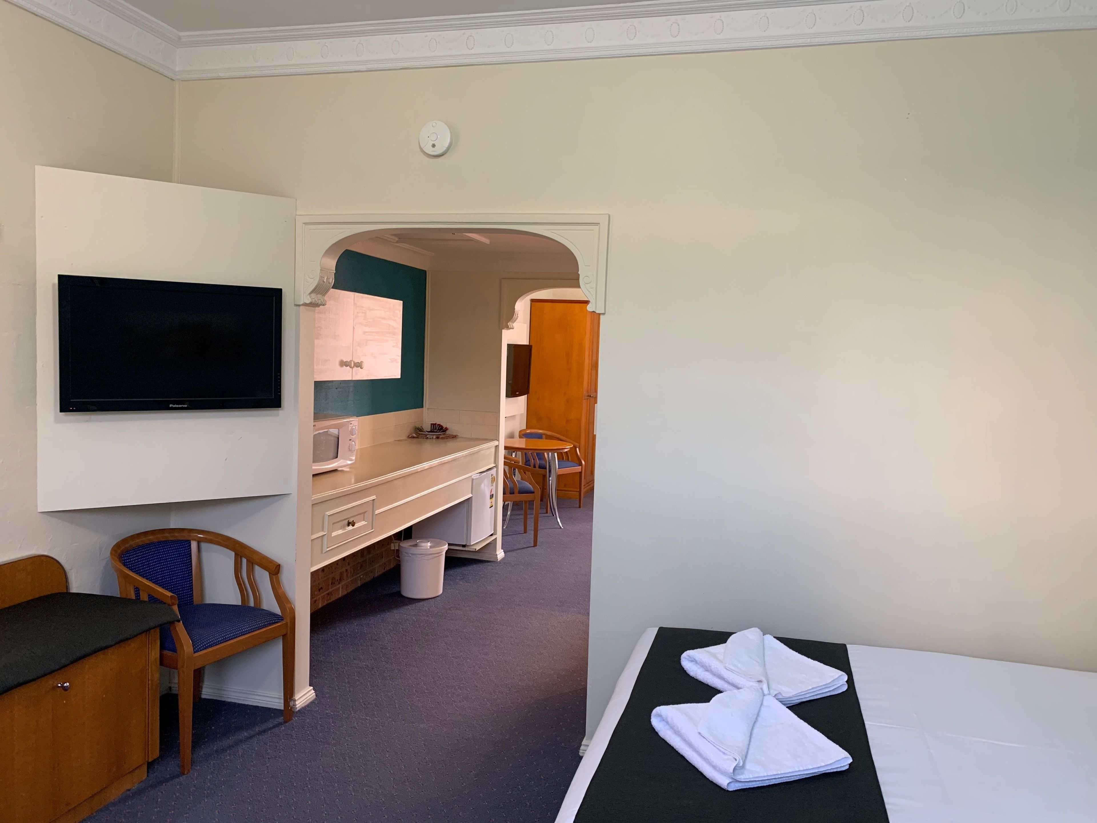 Une chambre d’hôtel comprenant un lit, un bureau avec une chaise, une télévision, une coiffeuse avec un miroir et une petite kitchenette.