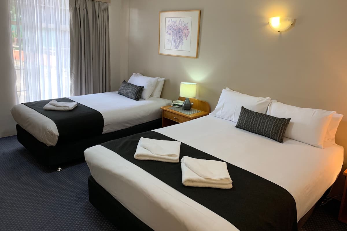 Two double beds with white and black bedding, a bedside table with a lamp, a framed picture on the wall, and a window with curtains.