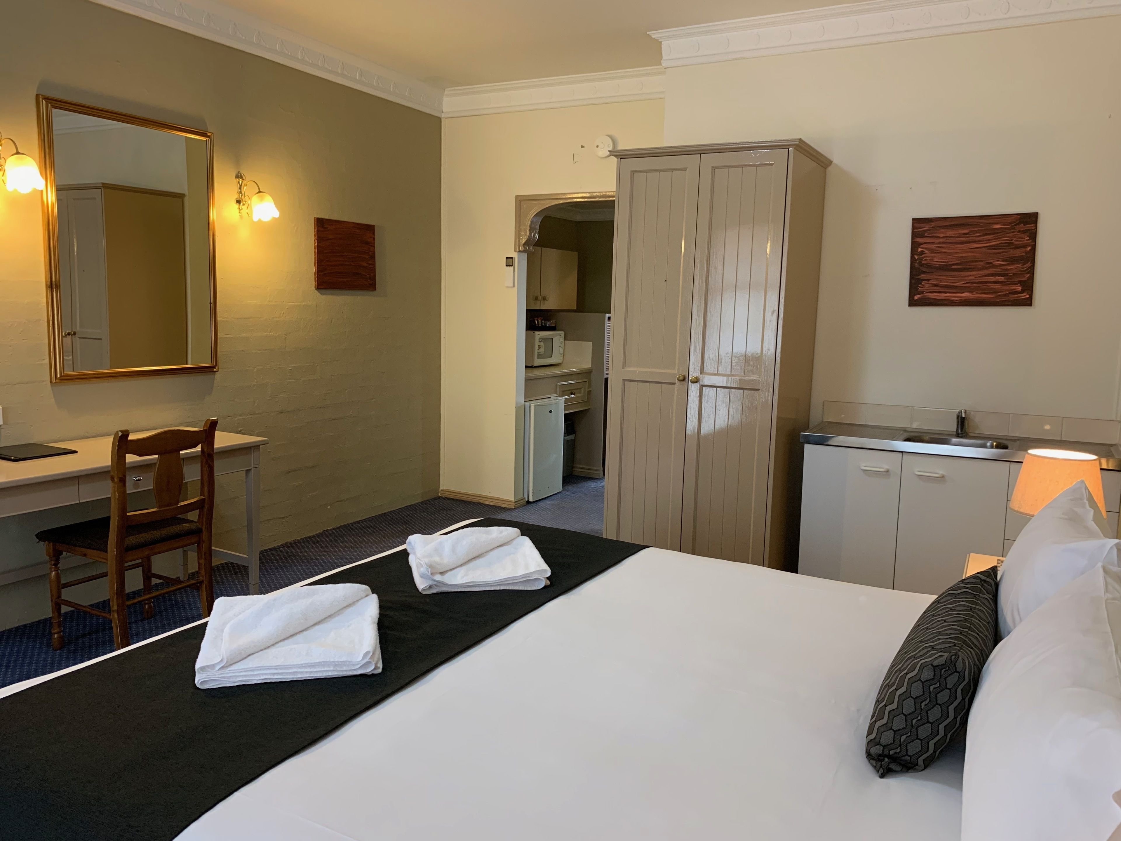 A hotel room with a bed, a desk, a chair, a wardrobe, and a kitchenette.
