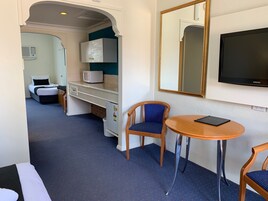 Habitación de hotel con cama, escritorio con microondas, silla, mesita, televisor y espejo.
