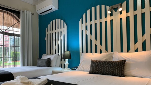 A hotel room with two beds, a large window, and a blue accent wall. - Heritage Motor Inn Goulburn (Goulburn)