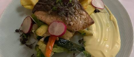A plate with a piece of grilled fish, lemon slices, radishes, and a creamy sauce.