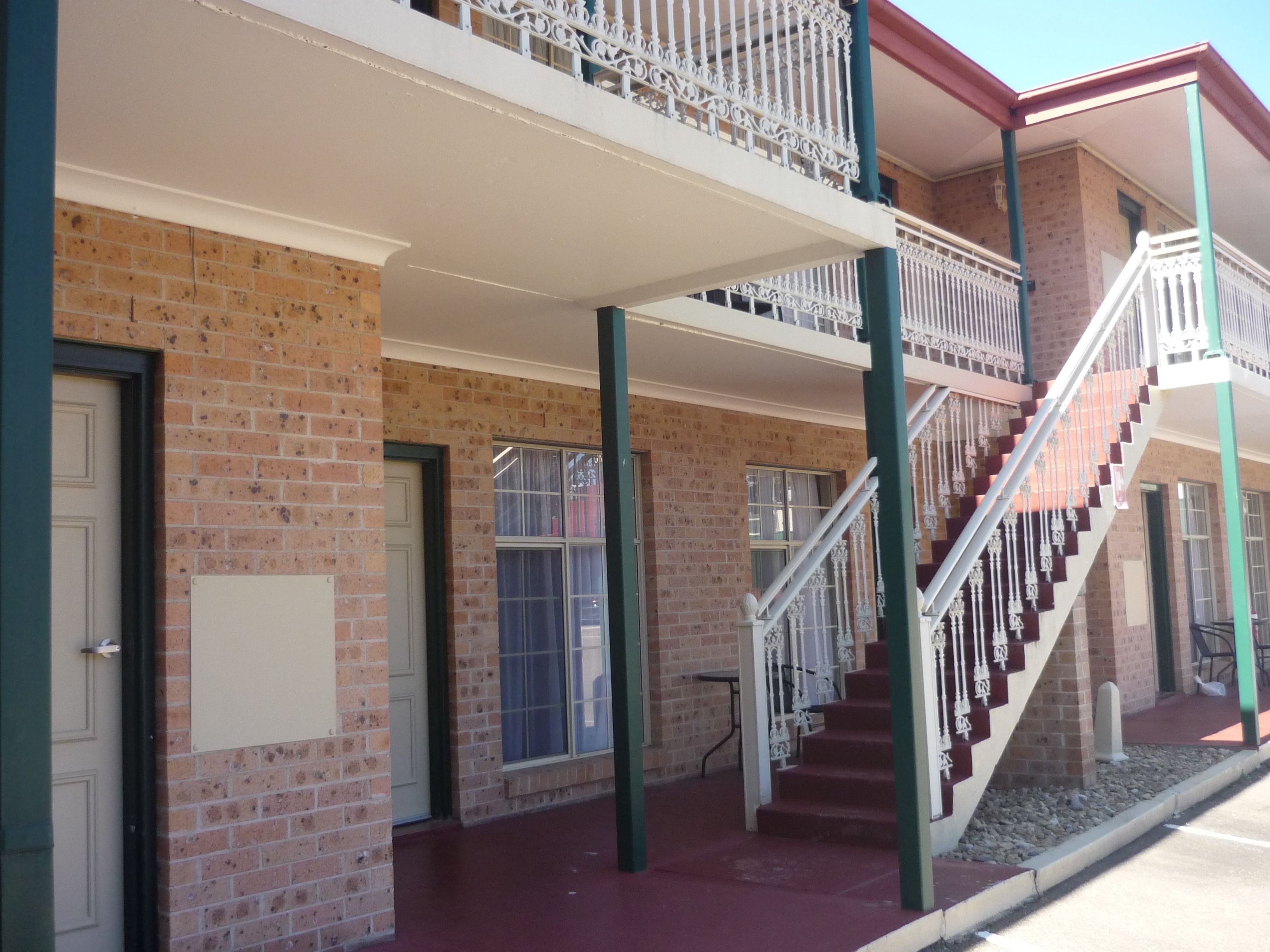 A two-story building with a brick facade, a balcony with white railings, and a staircase with white balusters.