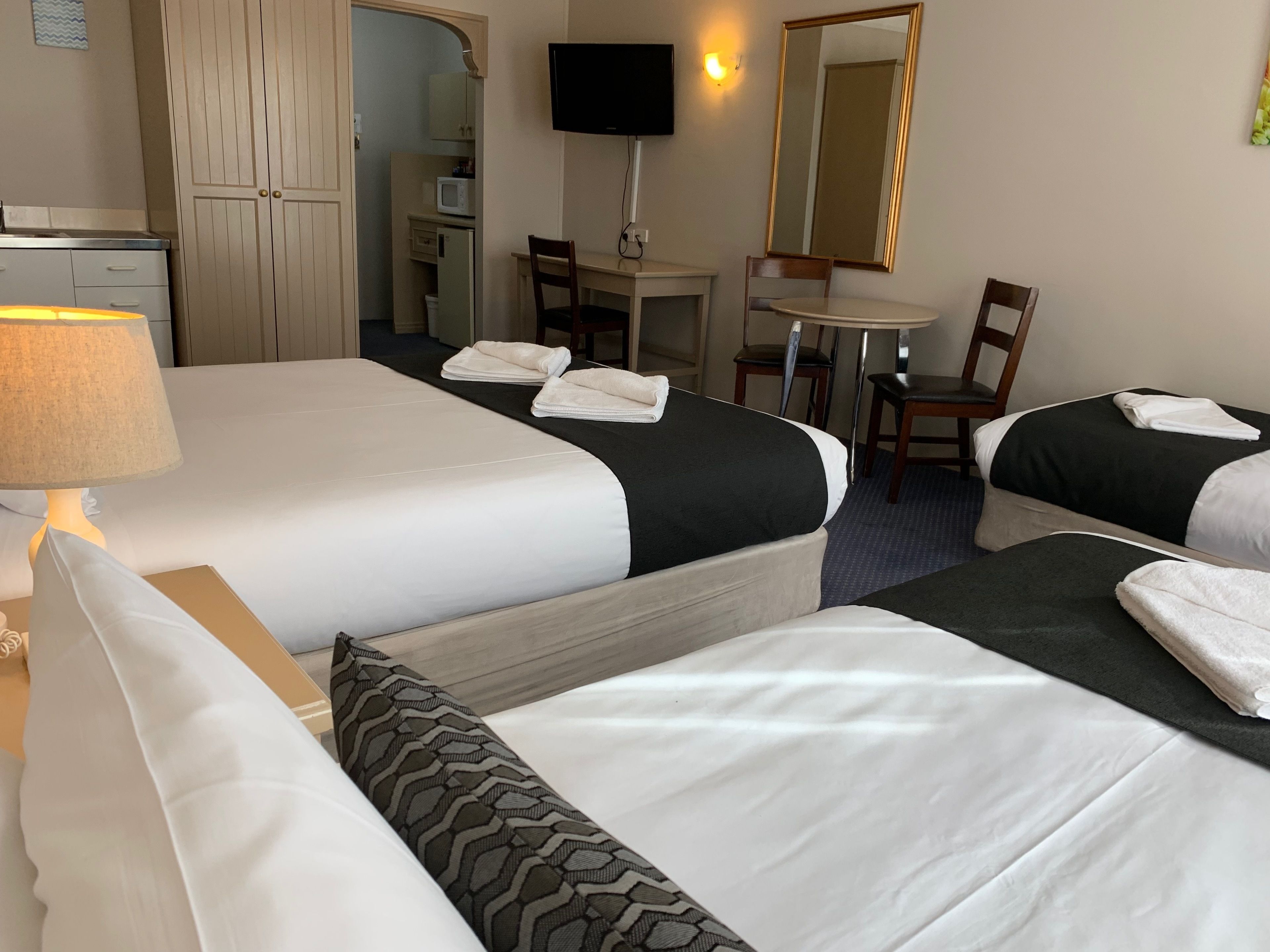 Una habitación de hotel con dos camas, un escritorio, una silla, un televisor y un espejo.