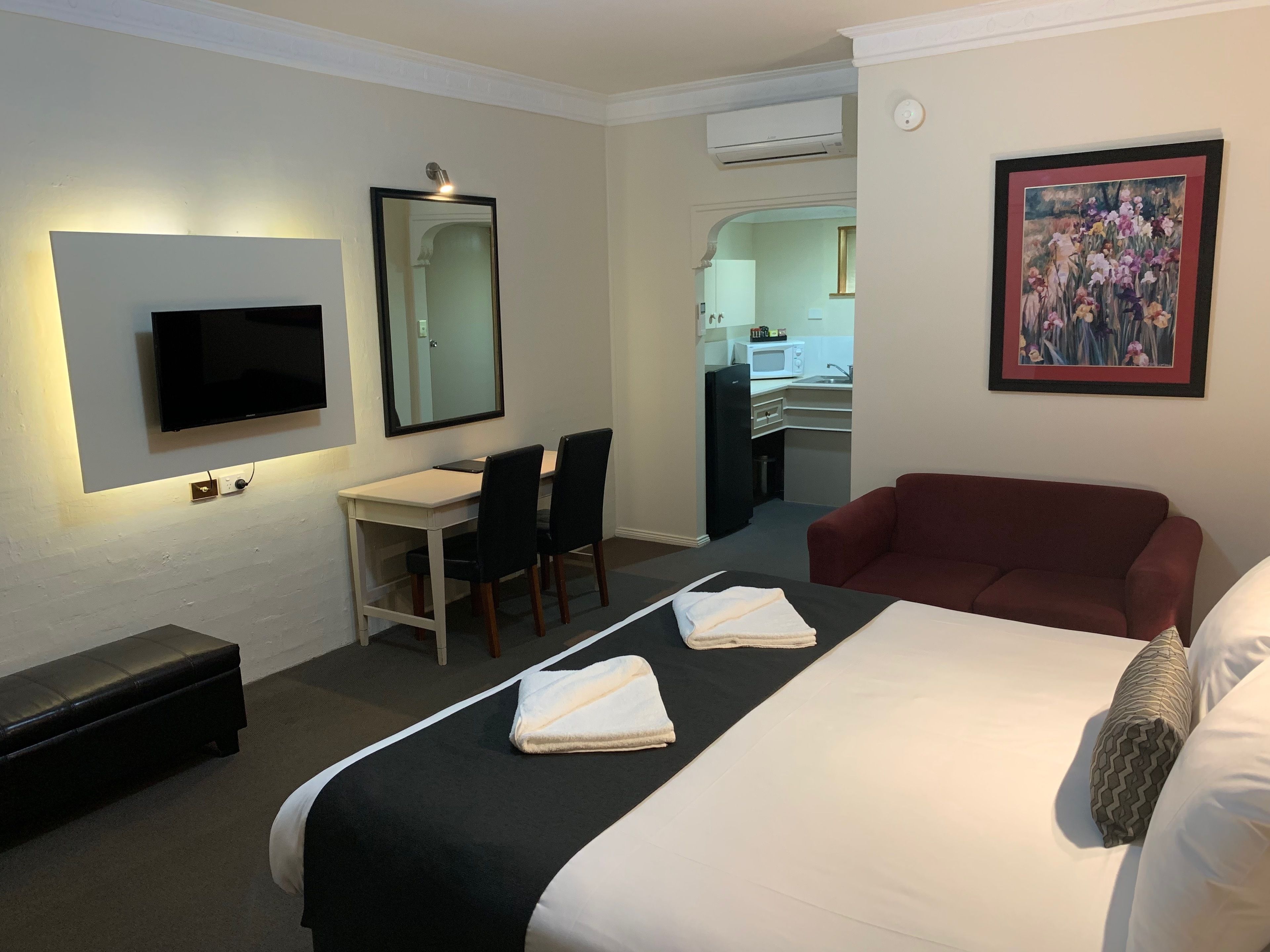Ein Hotelzimmer mit Bett, Schreibtisch, Stuhl, Fernseher, Spiegel, einer Couch und einem Gemälde.
