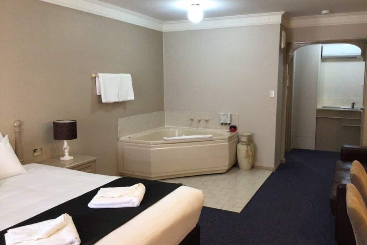 A hotel room with a bed, a large bathtub, a mirror, and a nightstand with a lamp.