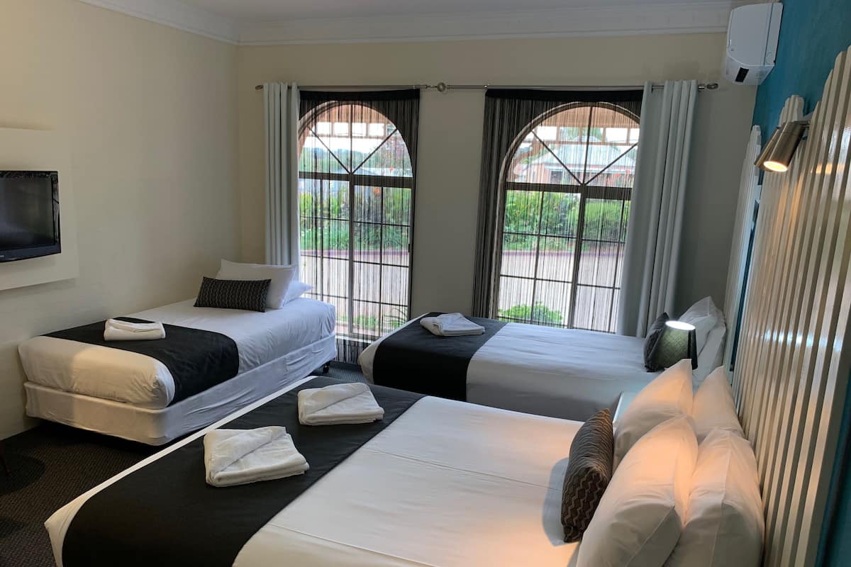 A hotel room with two beds, a flat-screen TV, and large windows with curtains.