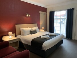 Habitación de hotel con una cama grande, dos mesitas de noche con lámparas, una pared roja, una ventana con cortinas y vistas a edificios.