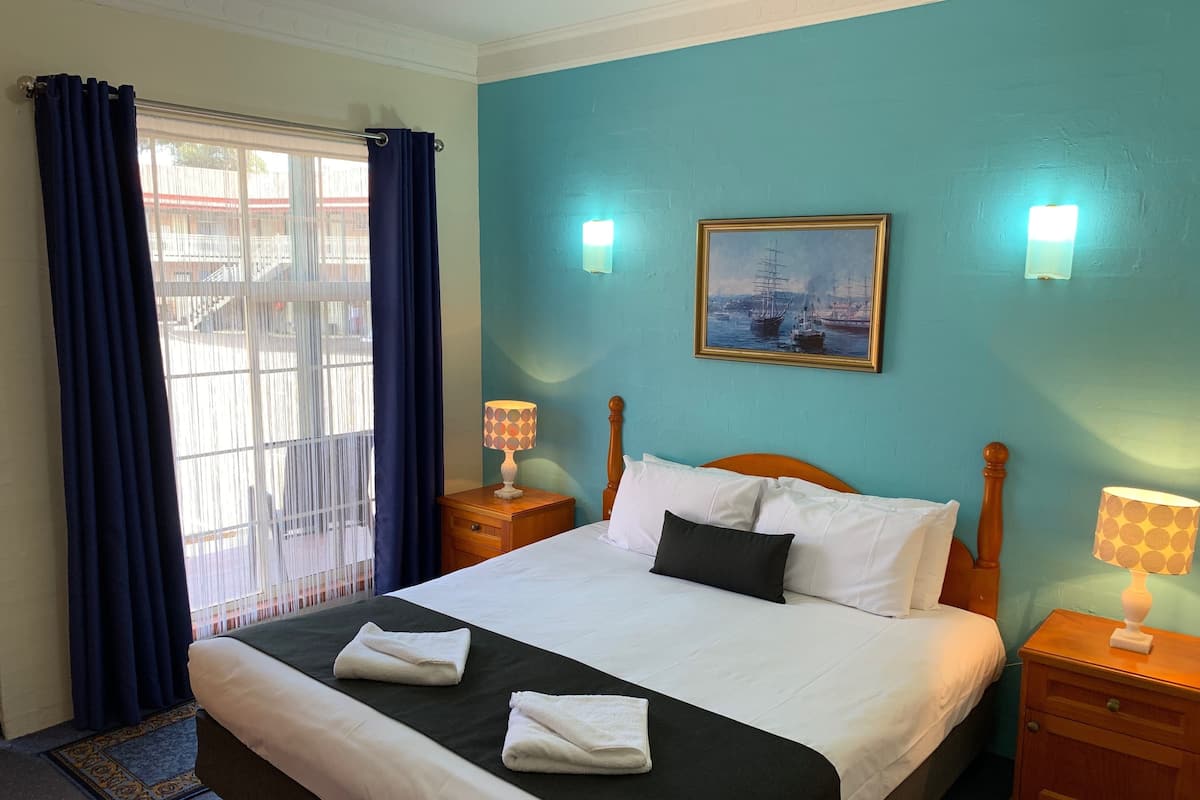 A neatly made bed with white and black linens, two bedside tables with lamps, a painting on the wall, and a window with blue curtains.