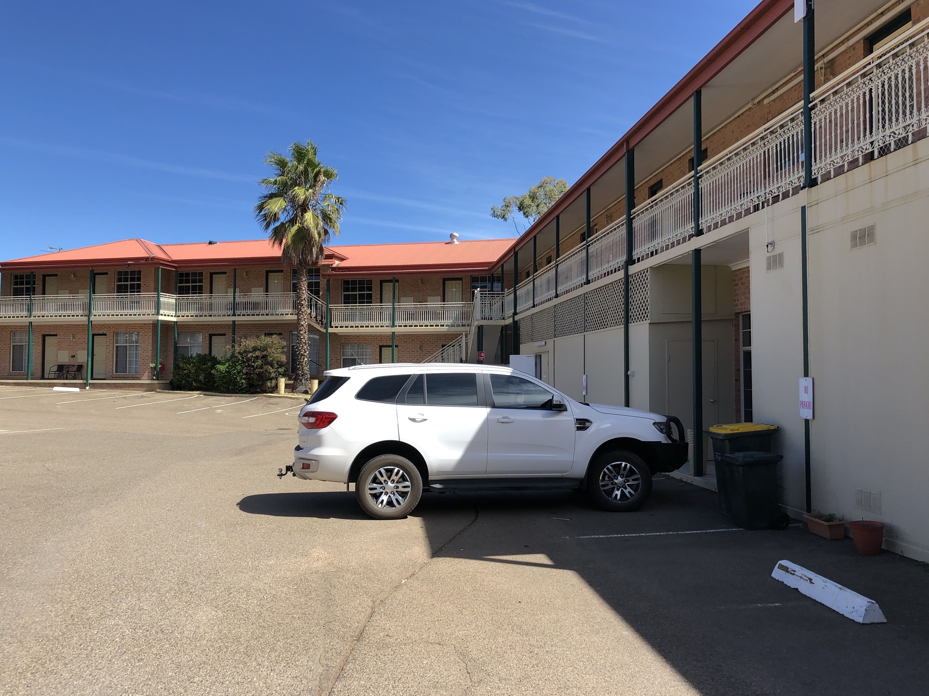 En hvid SUV parkeret på en parkeringsplads foran en bygning med rødt tag og altaner.