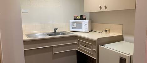 Una kitchenette compacta con microondas, lavamanos y pequeño refrigerador.