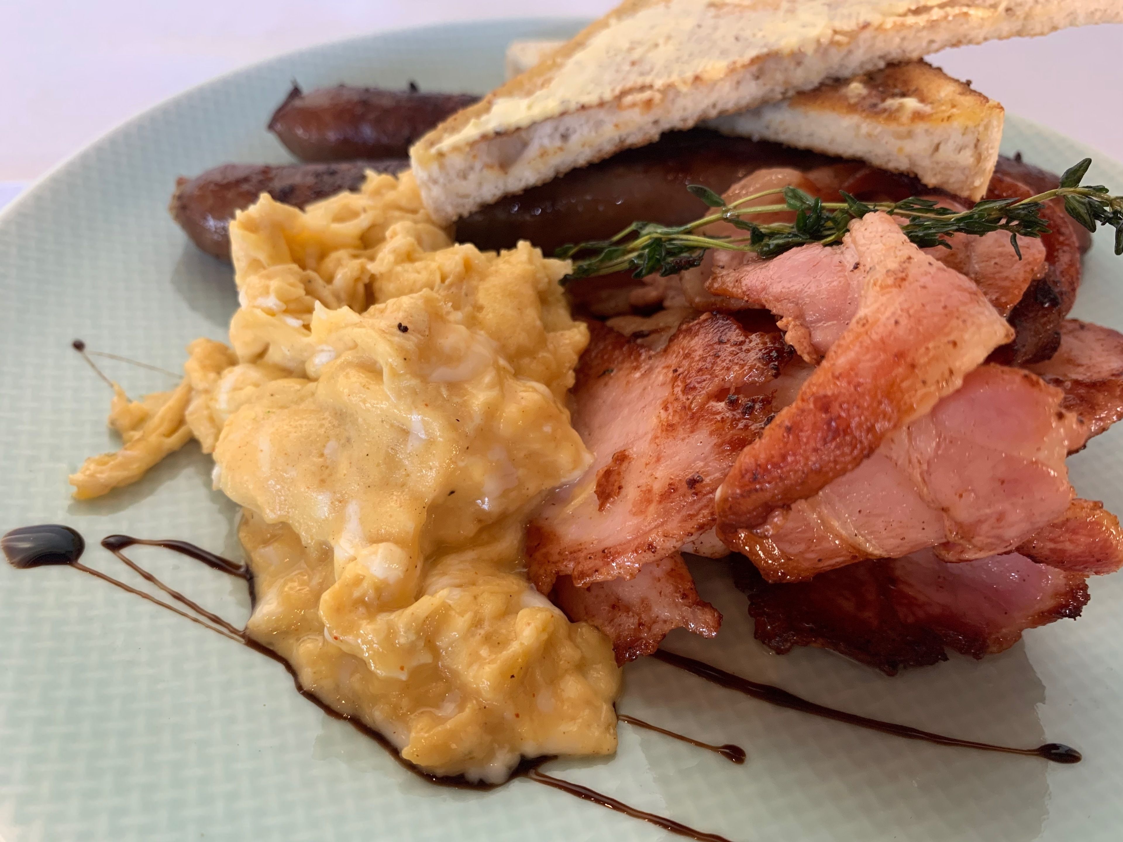 Une assiette d’œufs brouillés, de bacon, de saucisses et de pain grillé, garnie d’une branche de thym.