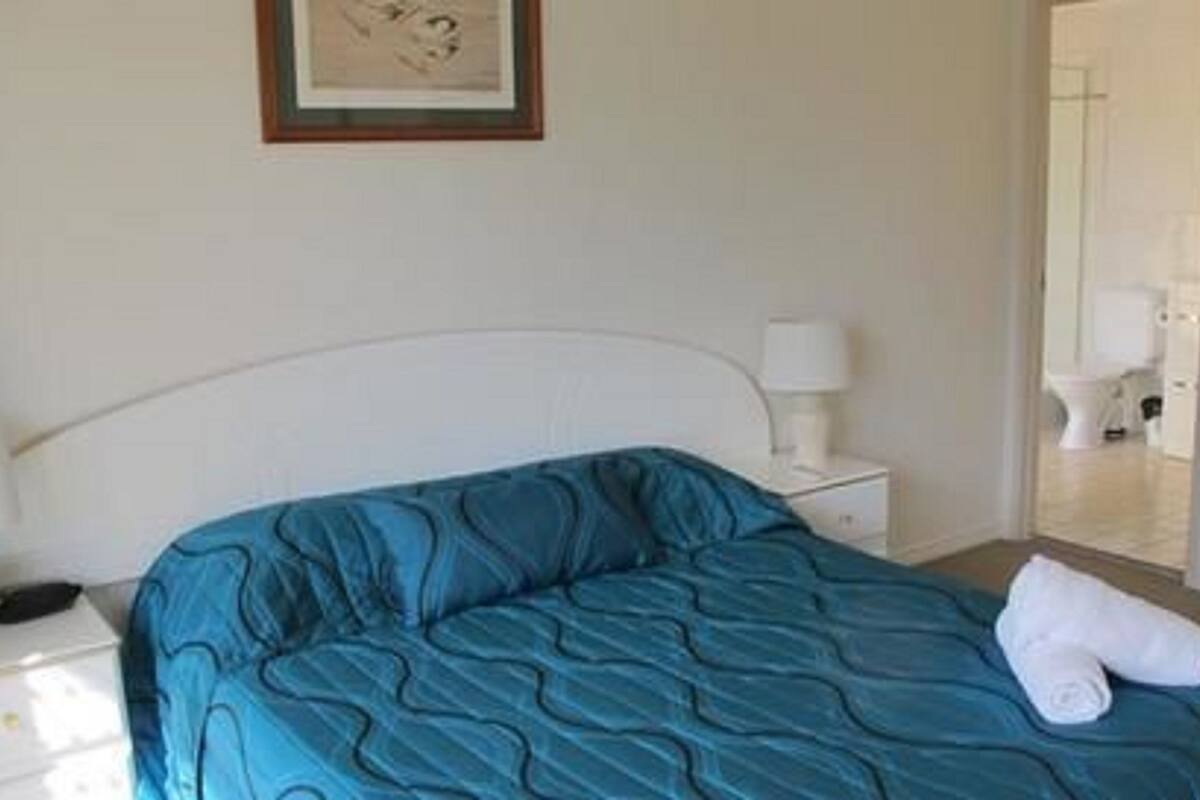 A bedroom with a single bed, a bedside table, a lamp, and a framed picture on the wall.