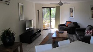A living room with a TV, sofa, coffee table, and a sliding glass door leading to a balcony.