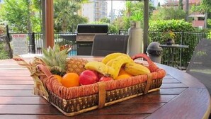 A fruit basket on a table with a view of a pool and outdoor seating.