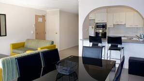 A living room with a sofa, chairs, a coffee table, and a kitchen area with a microwave, oven, and bar stools.