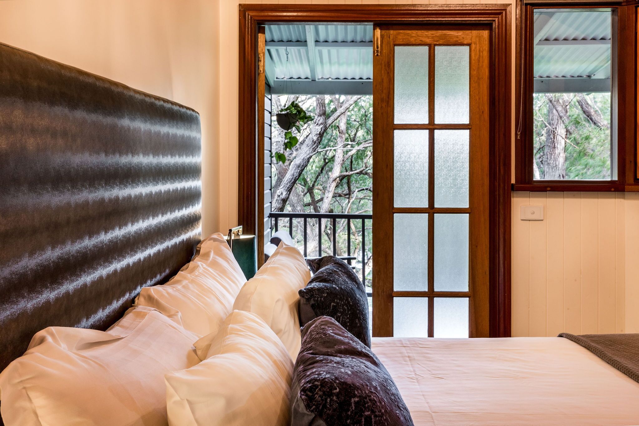 Un dormitorio con una cama grande, cabecera de madera y vistas a árboles a través de un ventanal.