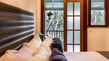 Un dormitorio con una cama grande, cabecera de madera y vistas a árboles a través de un ventanal.