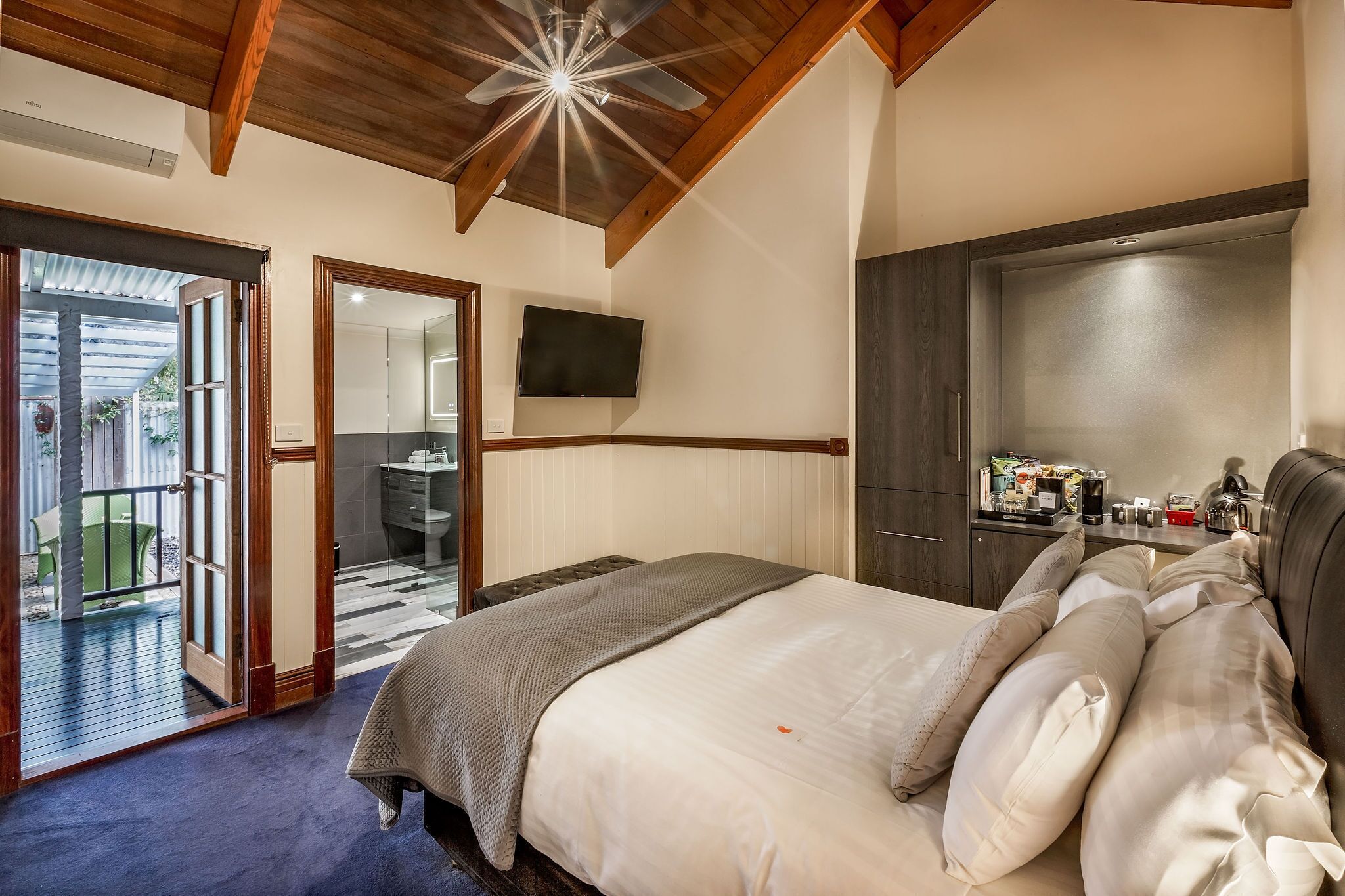 A bedroom with a large bed, a wooden ceiling, a flat-screen TV, and a sliding door leading to a balcony.