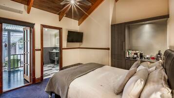 A bedroom with a large bed, a wooden ceiling, a flat-screen TV, and a sliding door leading to a balcony.