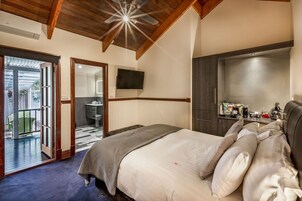 Un dormitorio con una cama grande, techo de madera, televisión de pantalla plana y puerta corredera que da a un balcón.