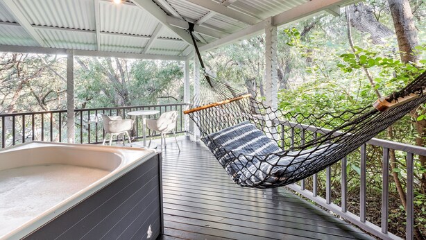 Una silla colgante con un cojín a rayas sobre una terraza de madera, un jacuzzi y una mesa con sillas.