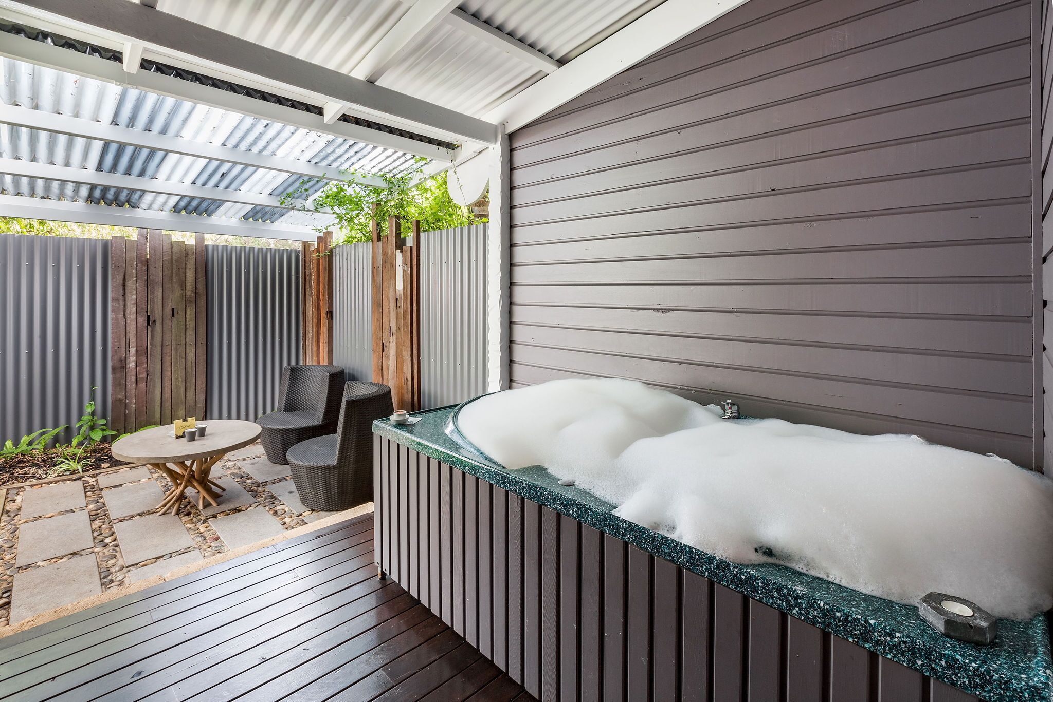 Een wellnessruimte met een jacuzzi, houten terras en buitenmeubilair.