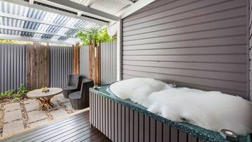 Een wellnessruimte met een jacuzzi, houten terras en buitenmeubilair.