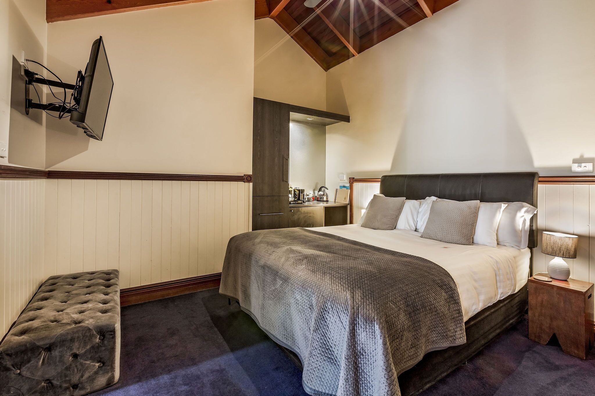 A bedroom with a bed, bedside table, and a television mounted on the wall.