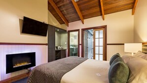 Un dormitorio con chimenea, una cama con almohadas, un televisor montado en la pared y un techo de madera.