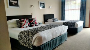 Een hotelkamer met twee bedden, elk met hoofdbord, een groot raam met gordijnen, en twee ingelijste foto's aan de muur.